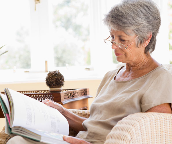 Older woman sitting on a couch reading a book.